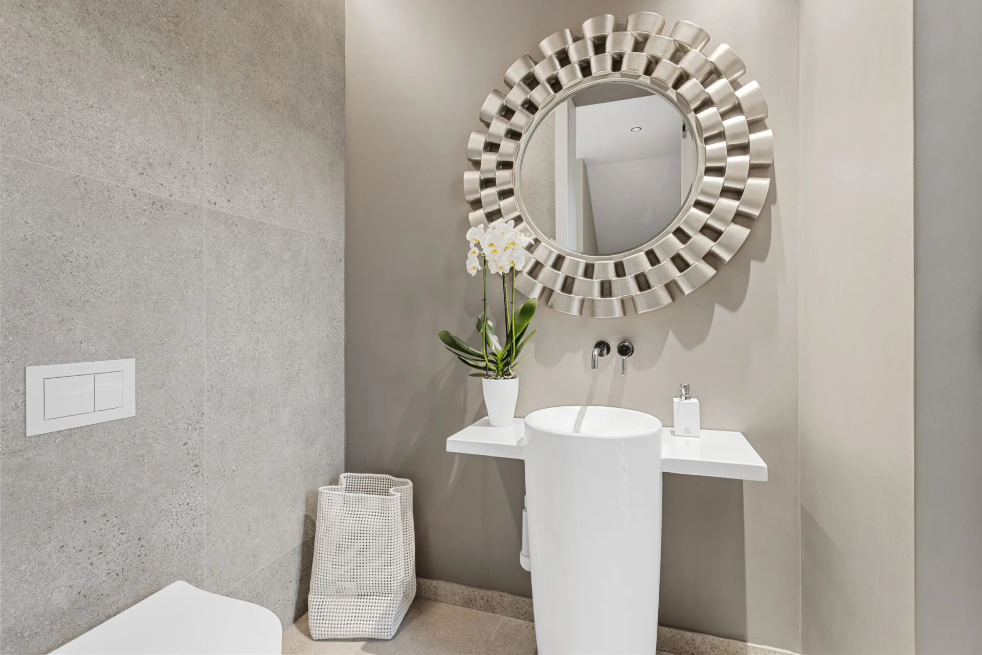 Gäste-WC mit Rundspiegel, freistehendem Waschbecken und Orchidee vor Steinfliesen