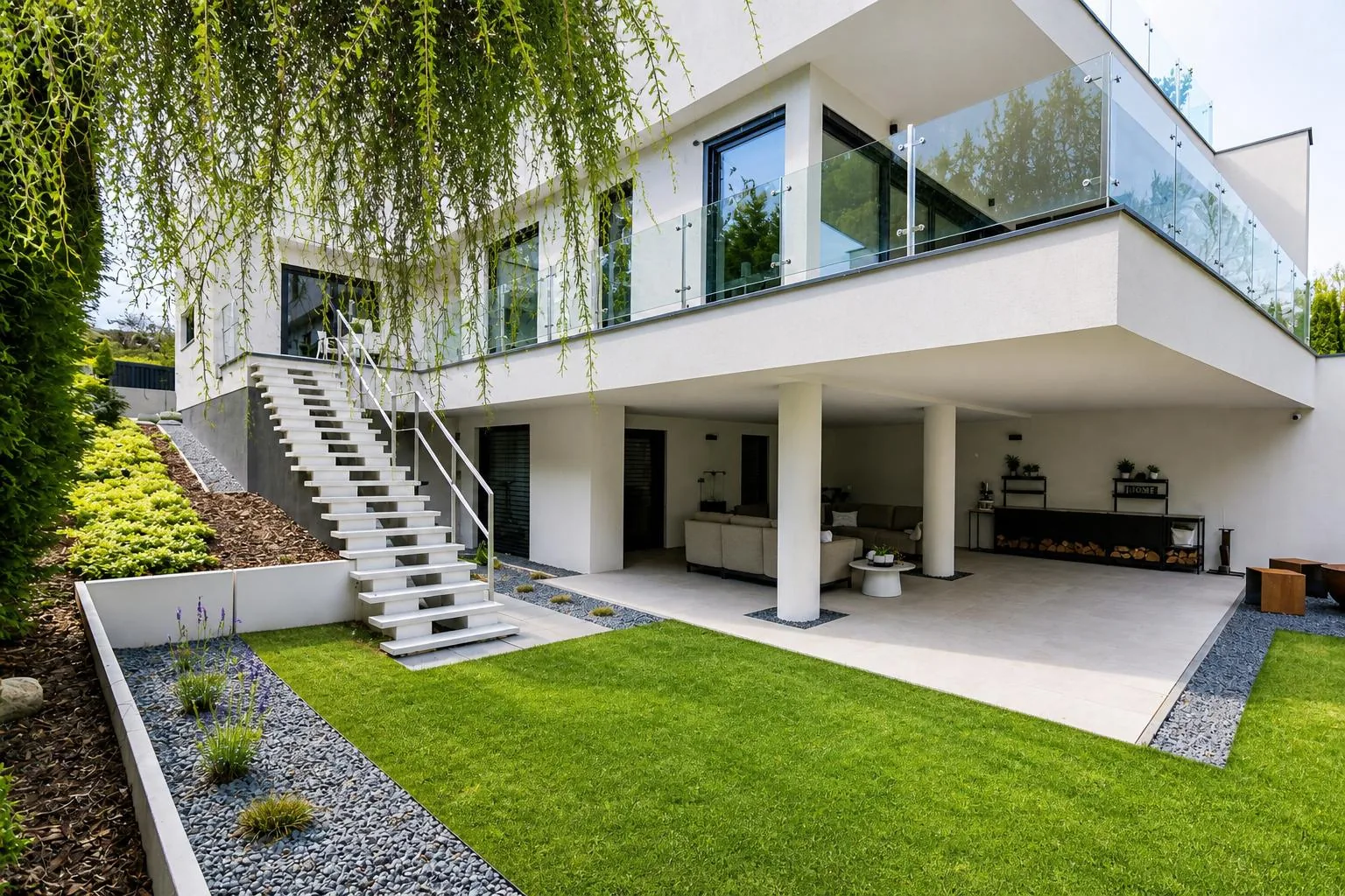 Weißes Wohnhaus mit Glasbrüstung, Außentreppe und überdachtem Sitzbereich zum Garten