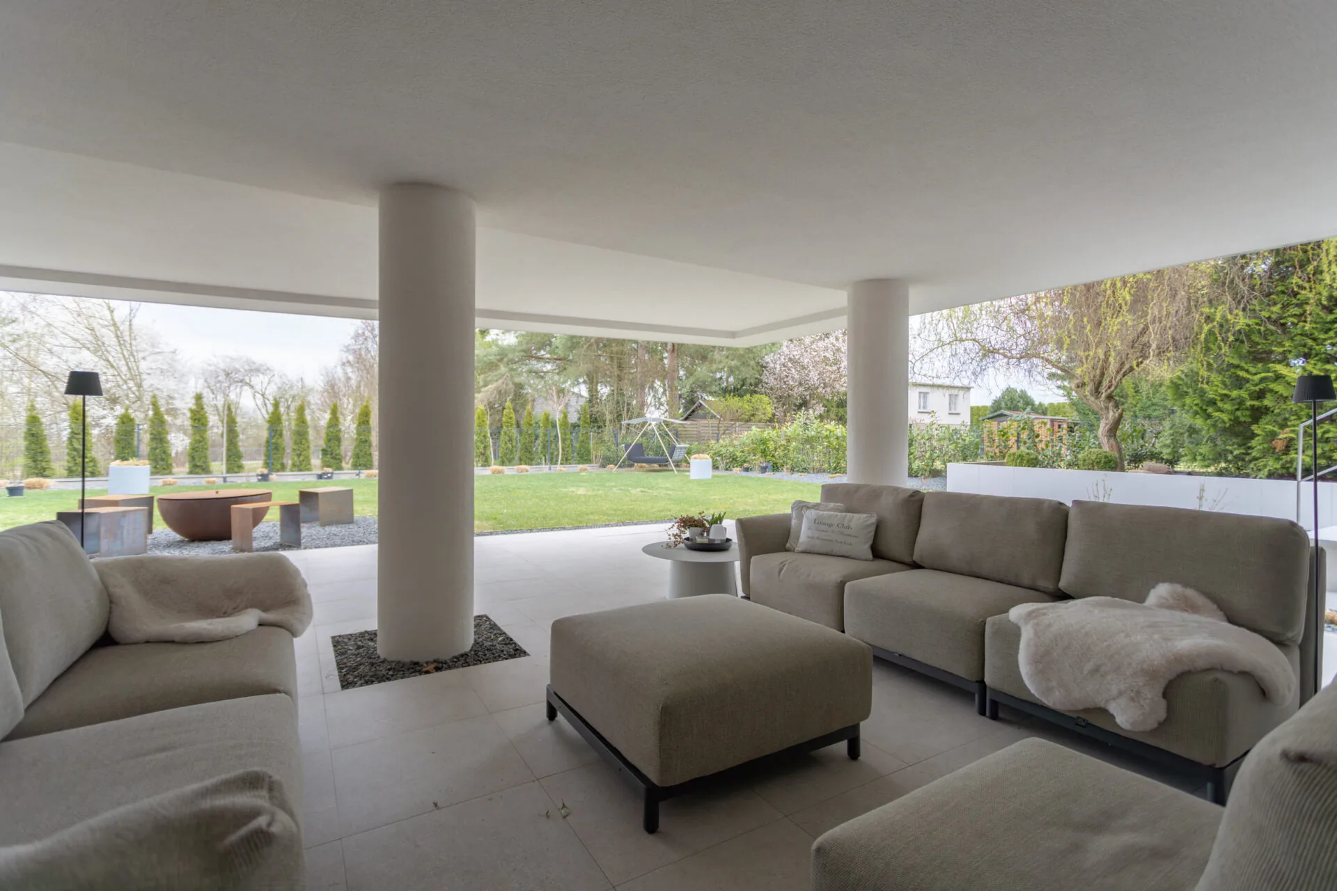 Überdachte Lounge mit hellen Sofas und Blick in den Garten